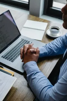 Hands at a laptop on a desk with a notebook and coffee